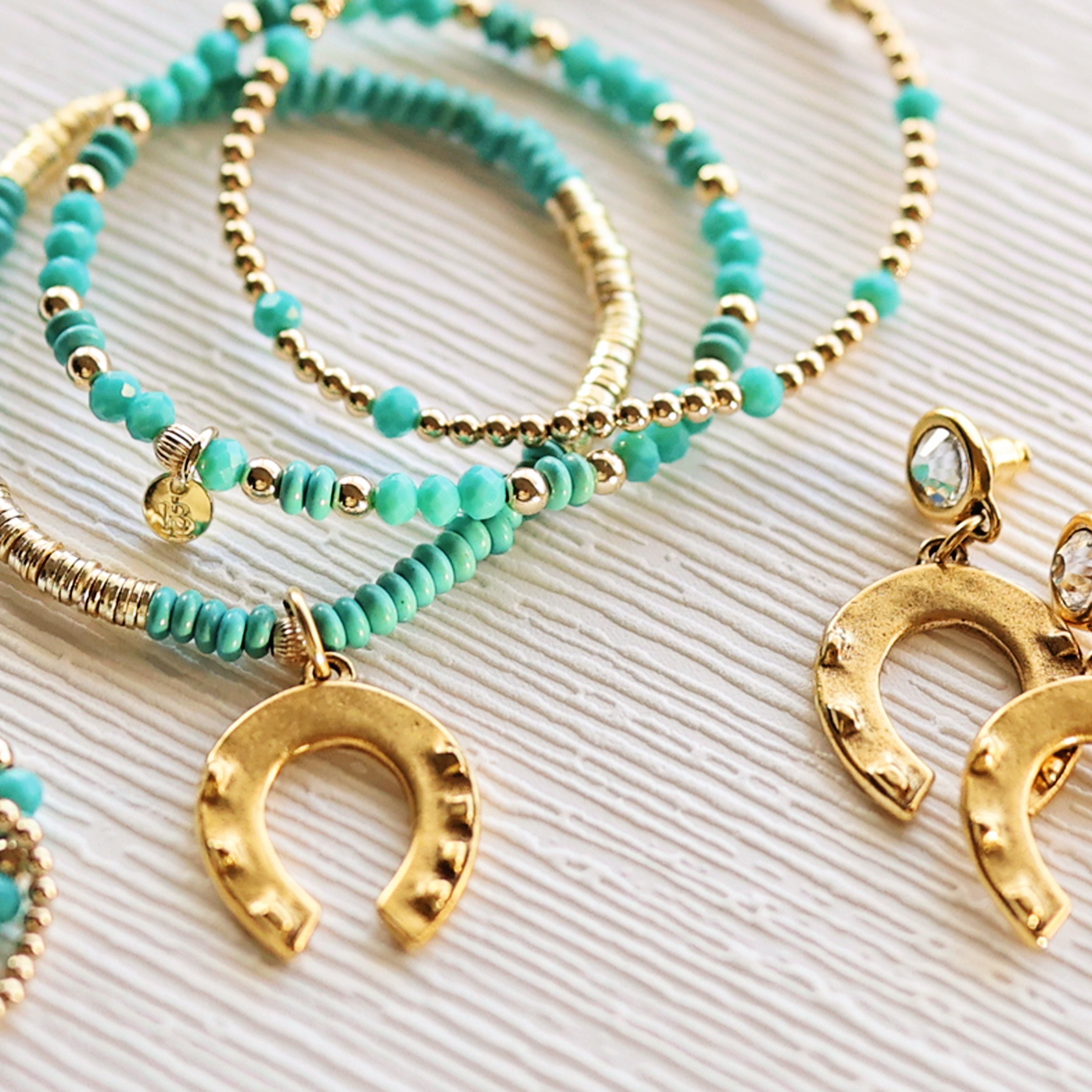Turquoise beaded bracelets with gold horseshoe charms on a textured surface