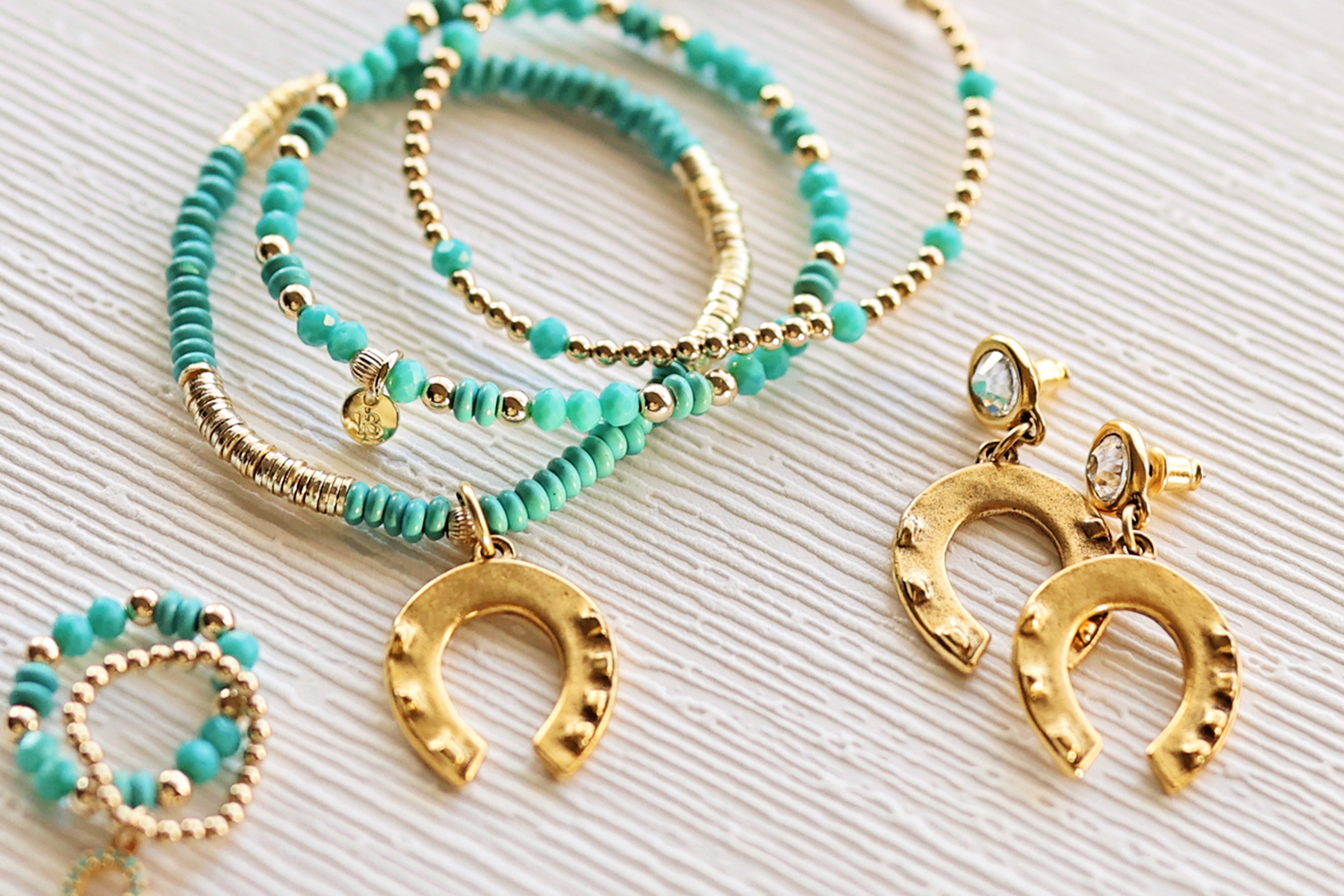 Turquoise beaded bracelets with gold horseshoe charms on a textured surface
