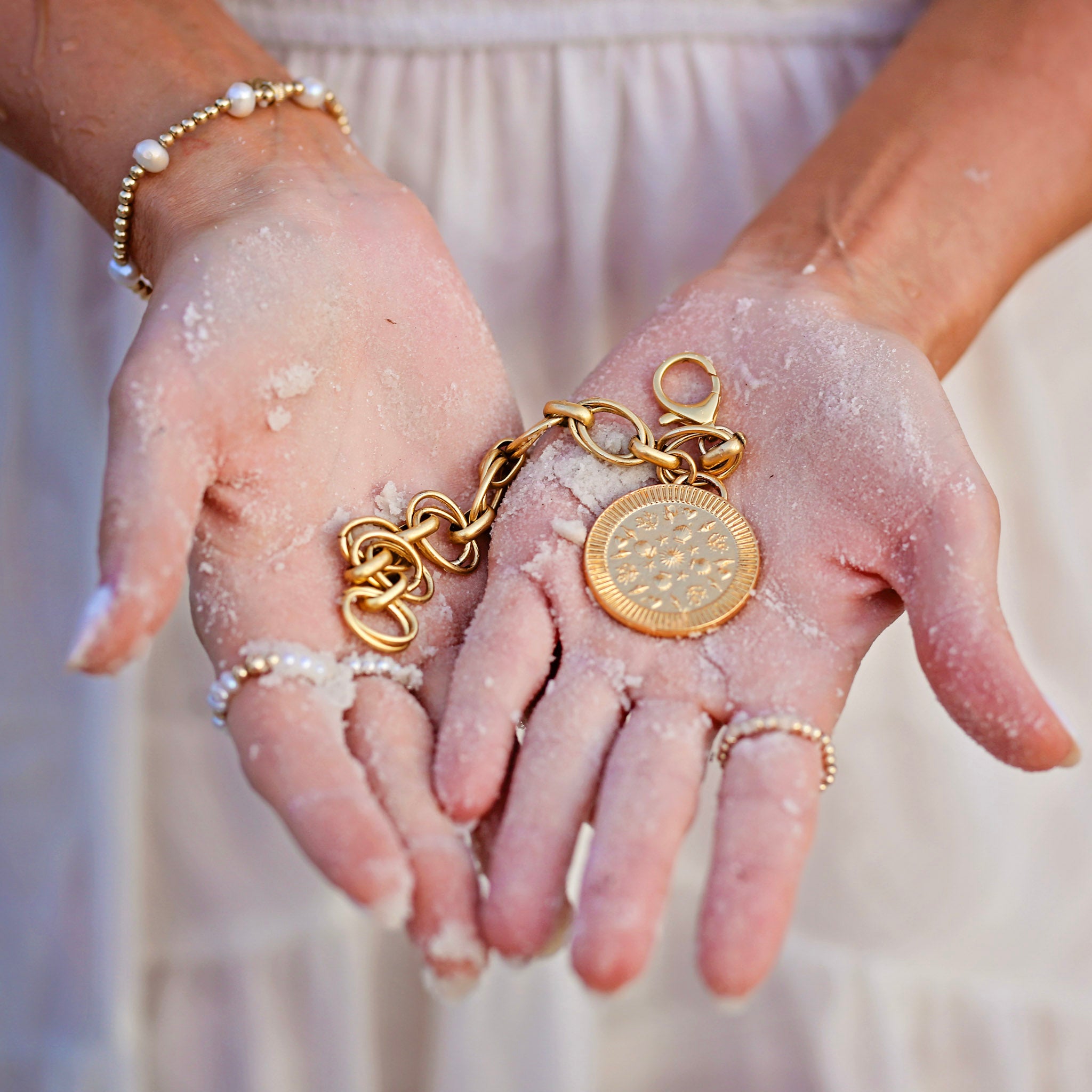 Hands with gold jewelry and sand on a blurred background