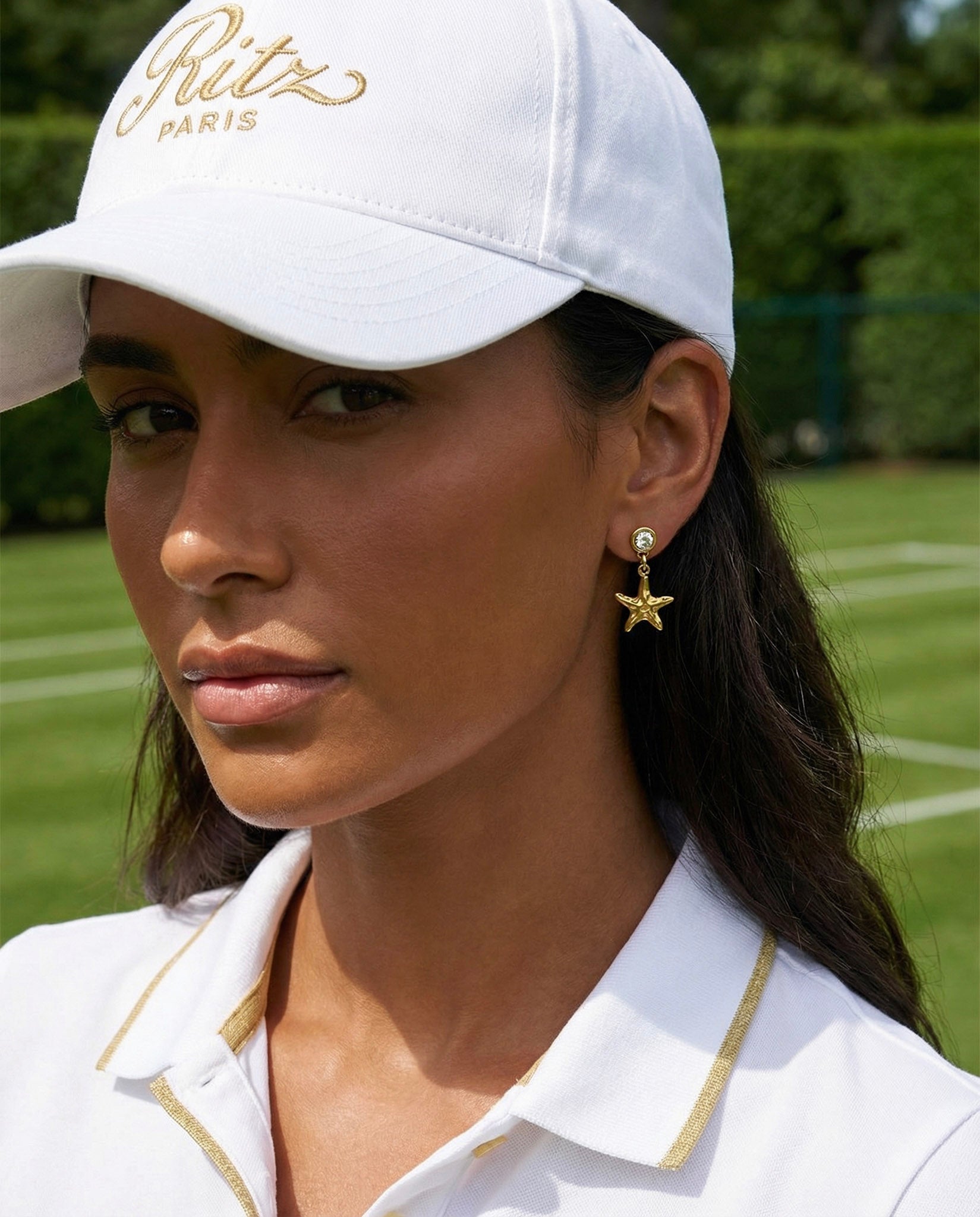 Woman wearing a white cap with 'Ritz Paris' branding and a white shirt on a grassy field.