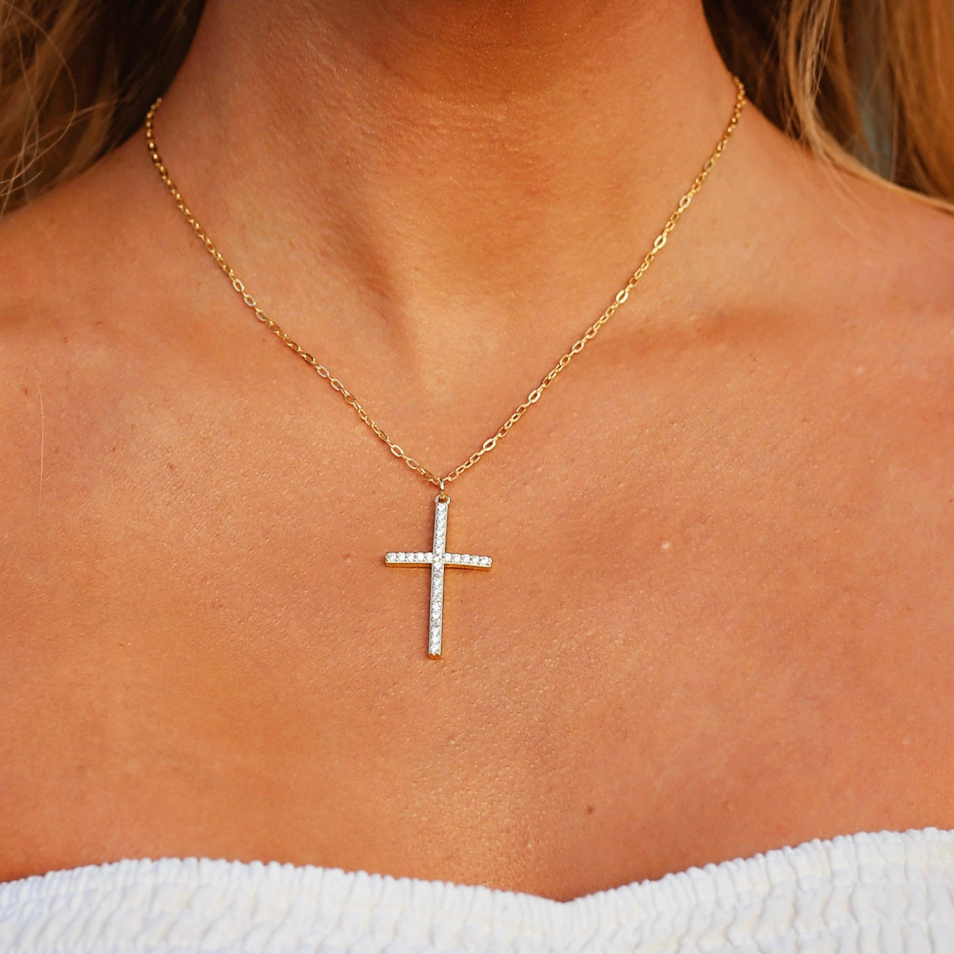 Gold necklace with a cross pendant on a person's neck