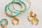 Turquoise beaded bracelets with gold horseshoe charms on a textured surface