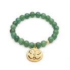 Green beaded bracelet with a gold four-leaf clover charm on a white background